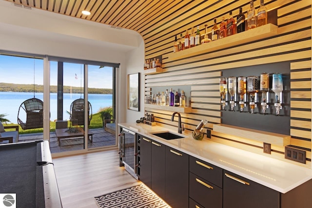 bar featuring beverage cooler, sink, a water view, and light wood-type flooring