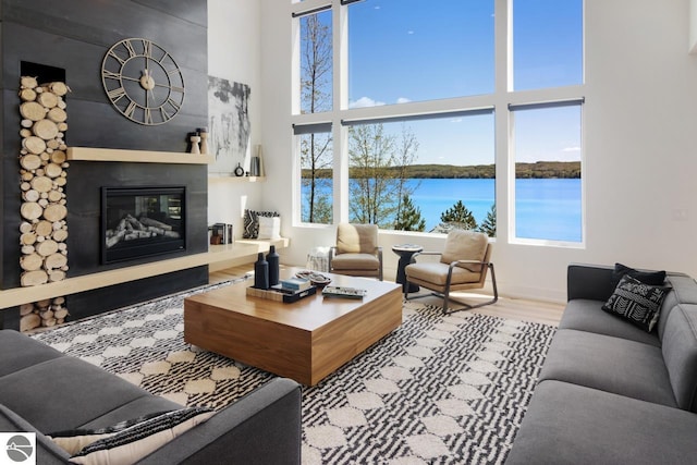 living room featuring light hardwood / wood-style flooring, a water view, and a high ceiling