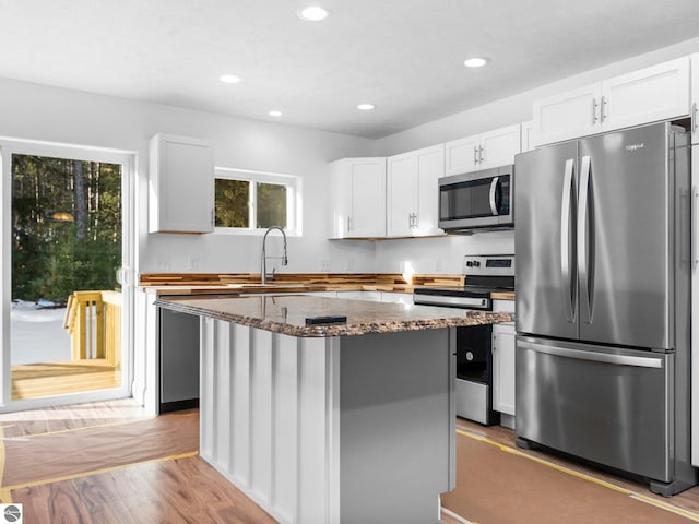 kitchen with appliances with stainless steel finishes, dark stone countertops, sink, a center island, and light wood-type flooring