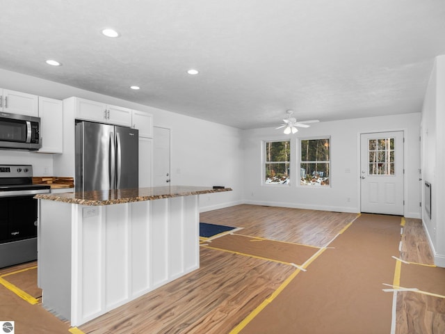 kitchen featuring light hardwood / wood-style flooring, ceiling fan, stainless steel appliances, dark stone countertops, and white cabinets