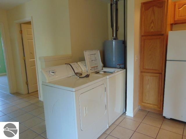 clothes washing area with light tile patterned flooring, washer and dryer, and gas water heater