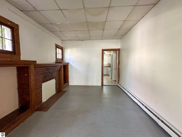 unfurnished living room featuring a drop ceiling, baseboard heating, a fireplace, and tile patterned flooring