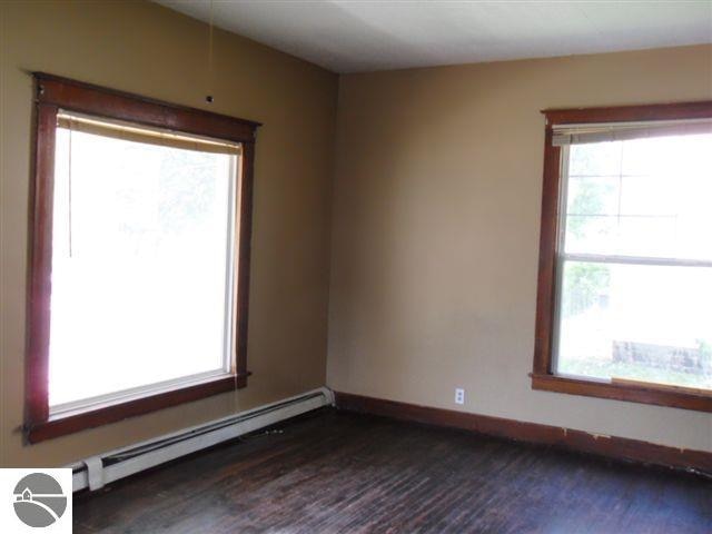 unfurnished room featuring a baseboard heating unit and dark hardwood / wood-style flooring