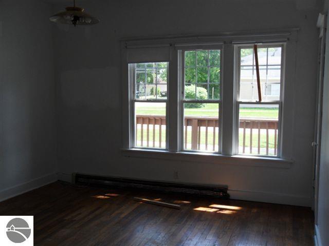 empty room featuring plenty of natural light, dark hardwood / wood-style floors, and a baseboard heating unit