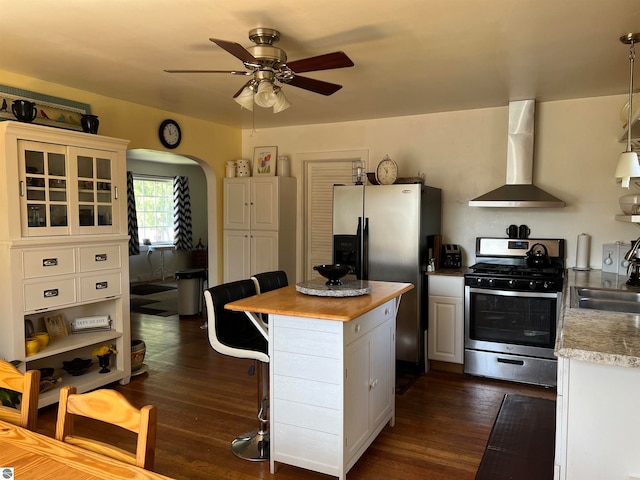 kitchen featuring stainless steel appliances, dark wood-type flooring, wall chimney range hood, a center island, and white cabinets