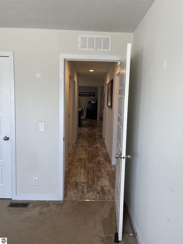 corridor with a textured ceiling, carpet flooring, visible vents, and baseboards