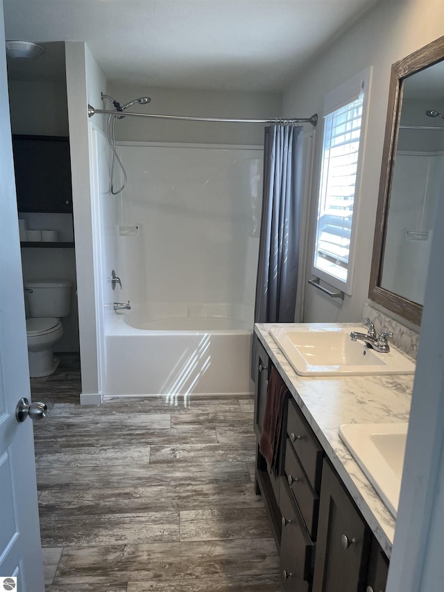 bathroom featuring double vanity, toilet, shower / tub combo with curtain, wood finished floors, and a sink