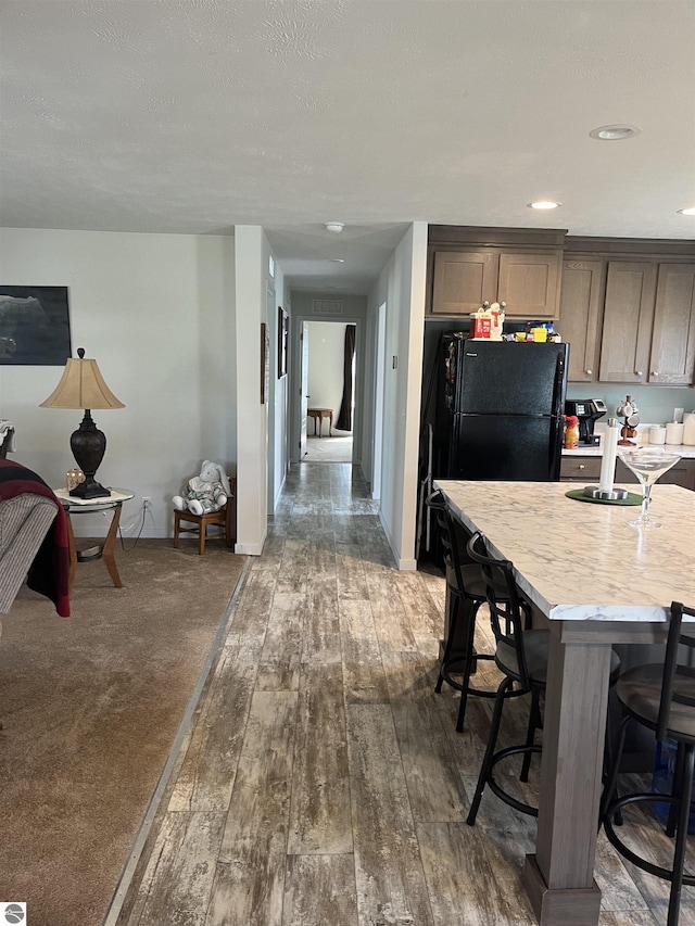 kitchen featuring dark wood-type flooring, baseboards, a kitchen breakfast bar, light countertops, and freestanding refrigerator