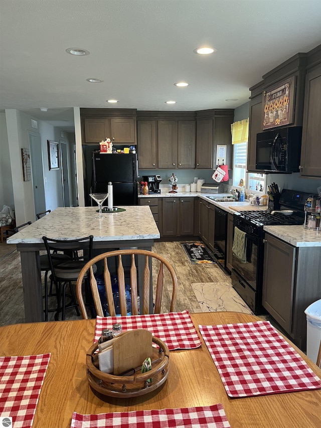 kitchen with recessed lighting, a sink, light countertops, a center island, and black appliances