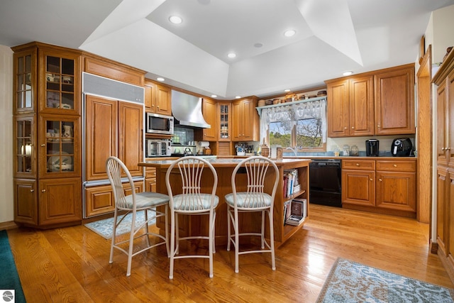 kitchen featuring a breakfast bar, light hardwood / wood-style flooring, a raised ceiling, and built in appliances