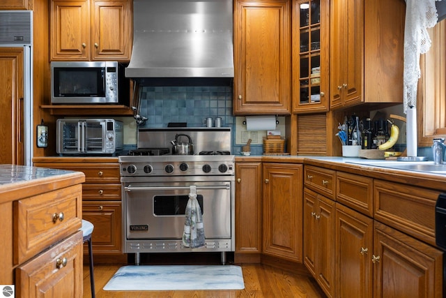 kitchen featuring backsplash, wall chimney range hood, high end appliances, and light wood-type flooring