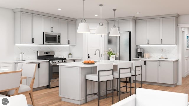 kitchen with stainless steel appliances, hanging light fixtures, light hardwood / wood-style floors, and a kitchen island with sink