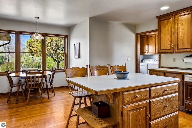 kitchen with pendant lighting, washer and clothes dryer, a center island, light wood-type flooring, and a kitchen bar