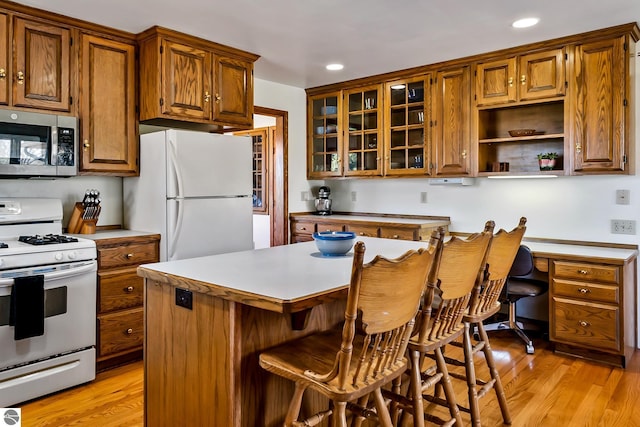 kitchen with a breakfast bar, a kitchen island, white appliances, and light wood-type flooring