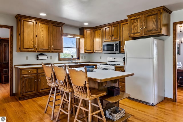 kitchen with a kitchen breakfast bar, white appliances, sink, light hardwood / wood-style flooring, and a center island