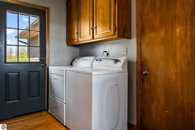 laundry area featuring a healthy amount of sunlight, washer and clothes dryer, cabinets, and light wood-type flooring