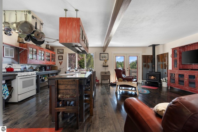 kitchen featuring a wood stove, white range with gas cooktop, beam ceiling, dark wood-type flooring, and french doors