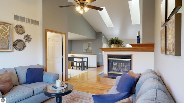 living room featuring high vaulted ceiling, hardwood / wood-style floors, ceiling fan, and a skylight