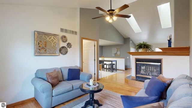 living room featuring high vaulted ceiling, hardwood / wood-style flooring, ceiling fan, and a skylight