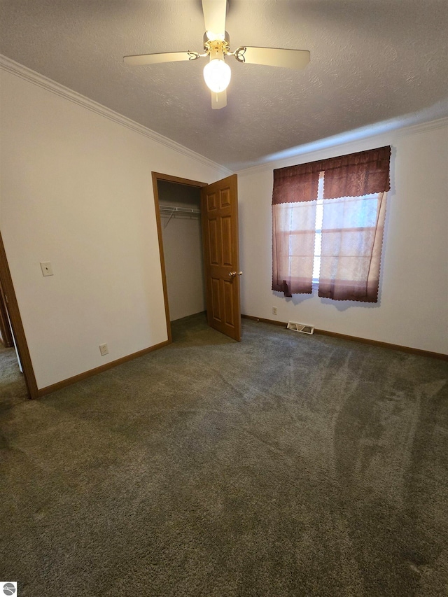 unfurnished bedroom featuring a textured ceiling, ornamental molding, a closet, ceiling fan, and dark carpet