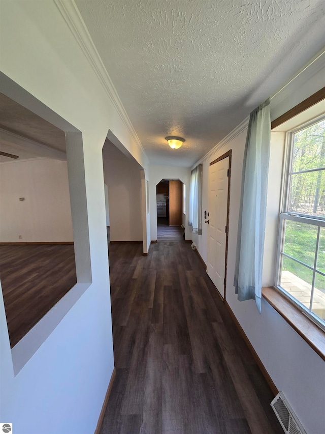 hallway with a healthy amount of sunlight, hardwood / wood-style flooring, ornamental molding, and a textured ceiling