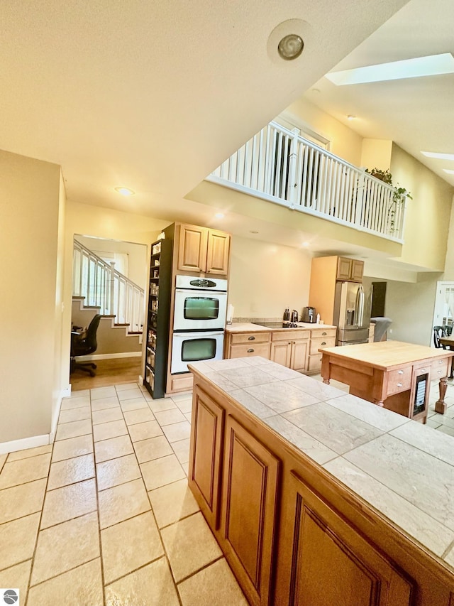 kitchen with stainless steel refrigerator with ice dispenser, double oven, light tile patterned floors, stovetop, and tile counters