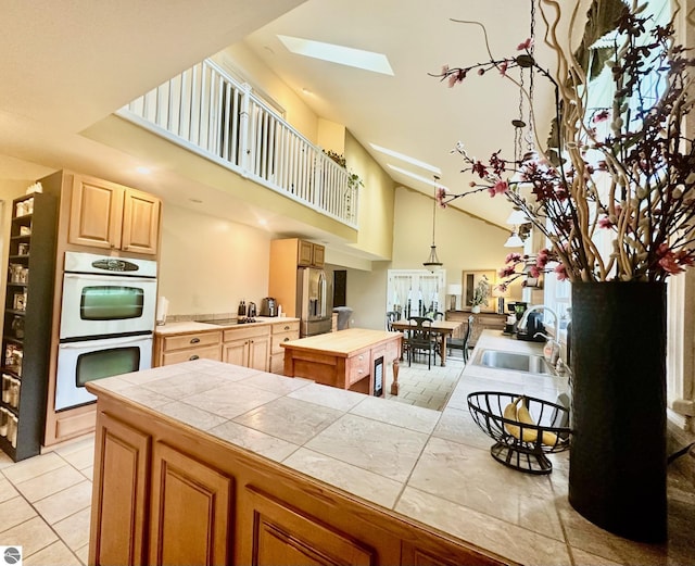 kitchen with stainless steel refrigerator with ice dispenser, a skylight, sink, tile counters, and black stovetop