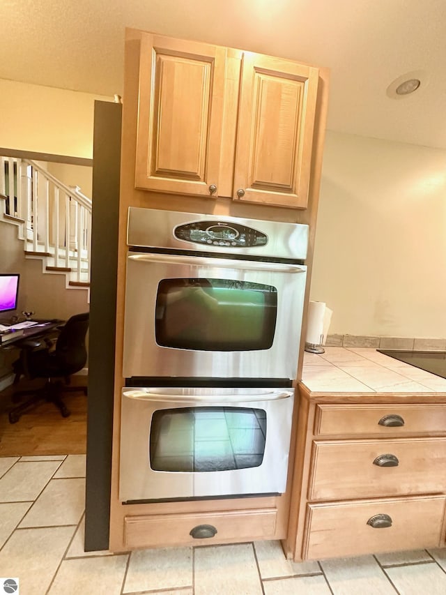 kitchen with tile countertops, light brown cabinets, light tile patterned floors, and double oven