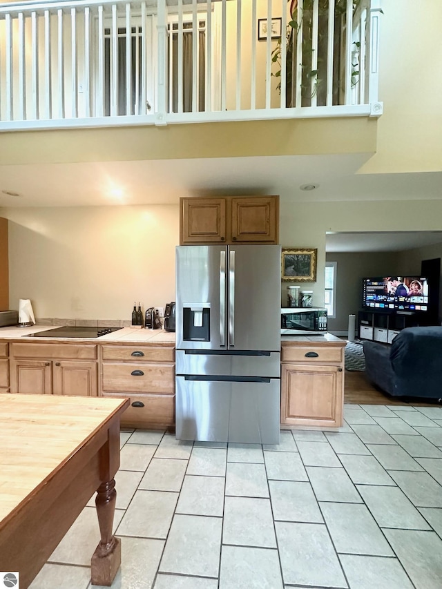 kitchen featuring stainless steel refrigerator with ice dispenser, a towering ceiling, black electric cooktop, and light tile patterned floors