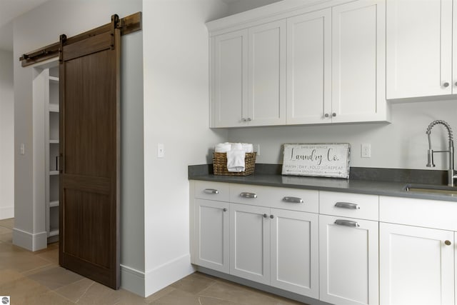 bar featuring sink, white cabinets, a barn door, and light tile patterned flooring