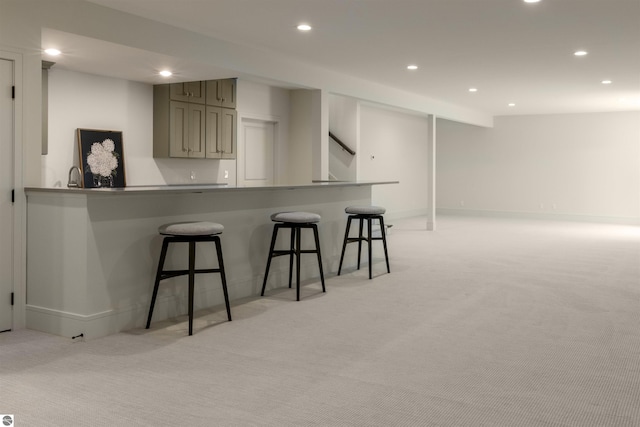 kitchen featuring gray cabinetry, light colored carpet, kitchen peninsula, and a kitchen bar