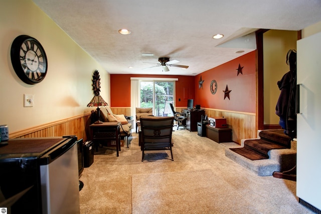 carpeted living room with a textured ceiling, ceiling fan, and wood walls