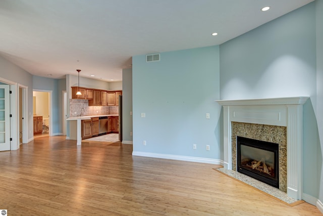 unfurnished living room featuring visible vents, baseboards, recessed lighting, a high end fireplace, and light wood finished floors