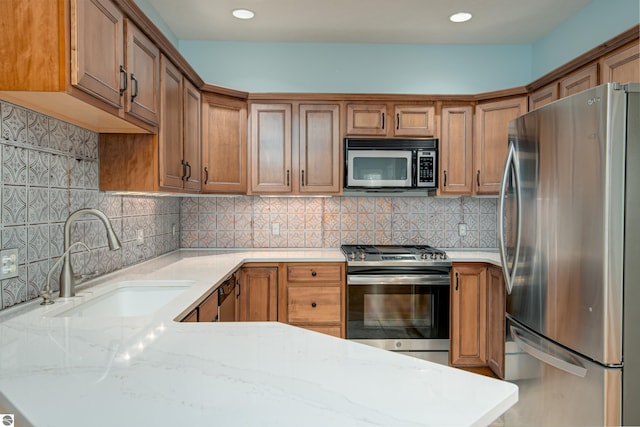kitchen featuring brown cabinetry, light stone countertops, recessed lighting, a sink, and appliances with stainless steel finishes