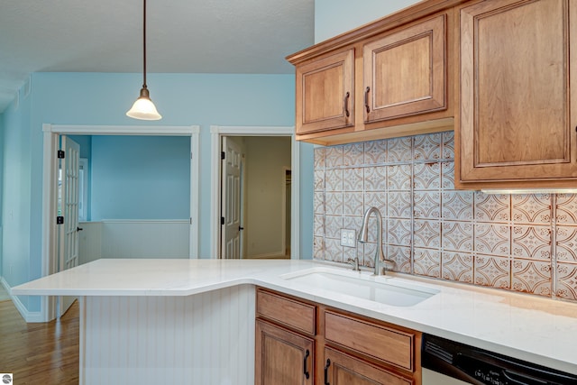 kitchen featuring dishwashing machine, brown cabinets, a sink, and decorative light fixtures
