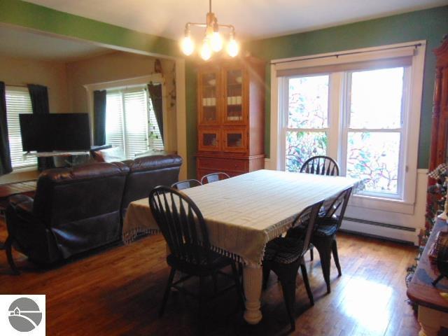 dining area with wood-type flooring, baseboard heating, a wealth of natural light, and a chandelier