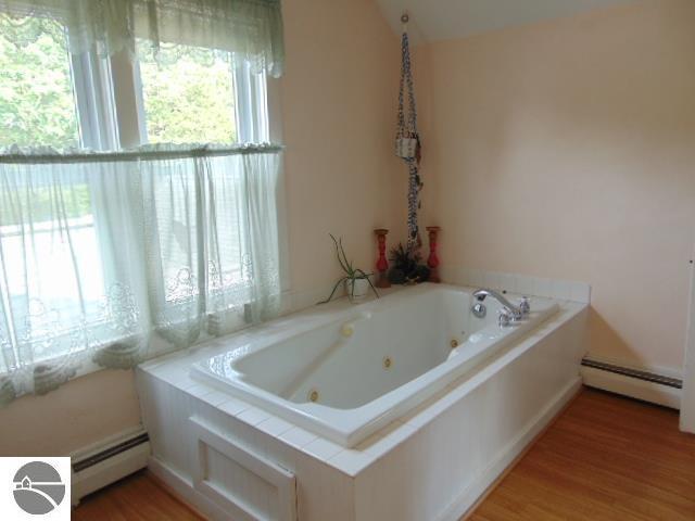 bathroom with hardwood / wood-style floors, a relaxing tiled tub, and baseboard heating