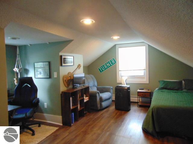 bedroom featuring a textured ceiling, a baseboard heating unit, vaulted ceiling, and hardwood / wood-style flooring