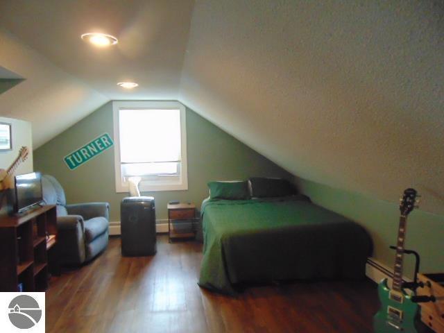 bedroom featuring lofted ceiling, dark wood-type flooring, and a baseboard heating unit