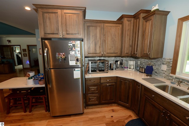 kitchen with tasteful backsplash, sink, stainless steel refrigerator, and light wood-type flooring