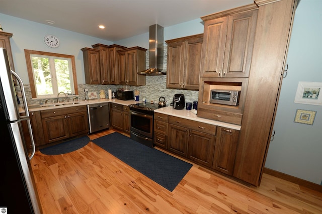 kitchen featuring appliances with stainless steel finishes, light hardwood / wood-style flooring, tasteful backsplash, sink, and wall chimney exhaust hood