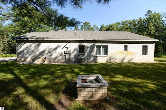 rear view of house featuring central AC unit, a yard, and an outdoor fire pit