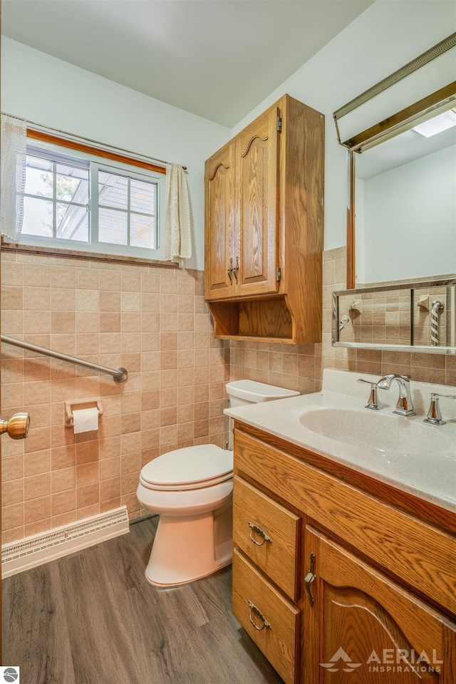 bathroom featuring a baseboard heating unit, toilet, vanity, tile walls, and hardwood / wood-style flooring