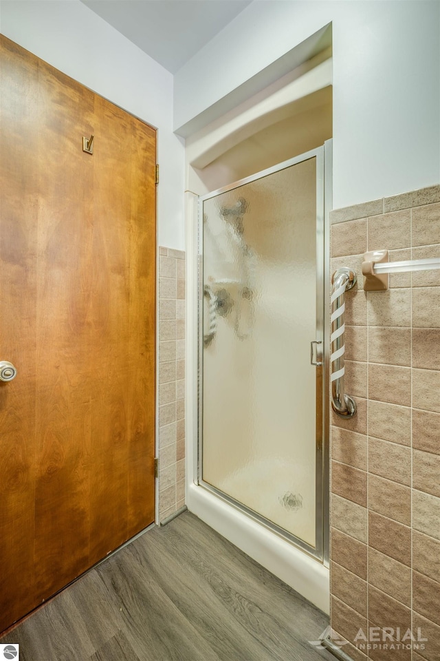 bathroom featuring hardwood / wood-style floors, tile walls, and a shower with shower door