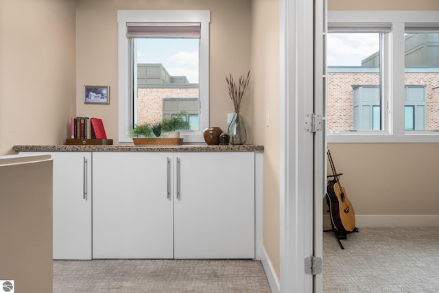 bar with stone counters, white cabinetry, a wealth of natural light, and light colored carpet