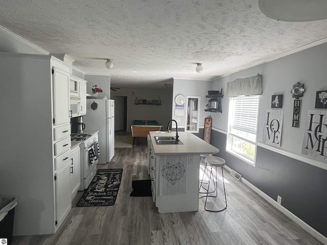 kitchen with sink, white appliances, a breakfast bar area, a kitchen island with sink, and white cabinets