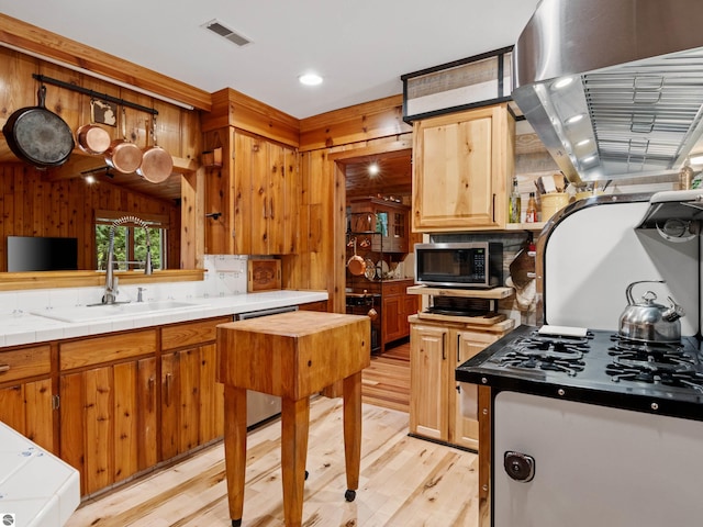 kitchen with tile counters, sink, wood walls, light hardwood / wood-style floors, and extractor fan