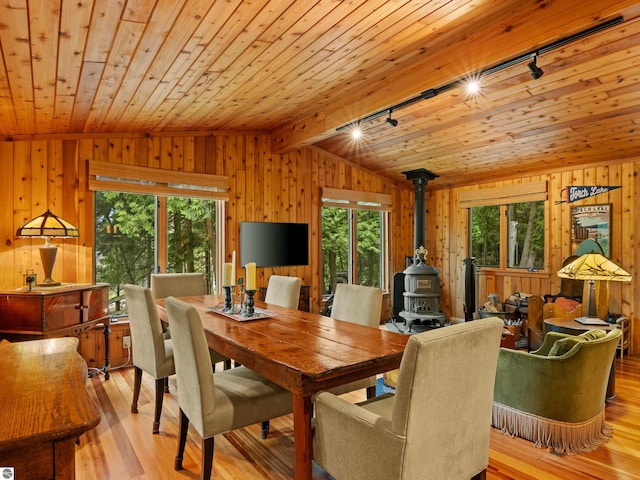 dining room featuring a wood stove, wooden ceiling, rail lighting, vaulted ceiling, and light hardwood / wood-style floors