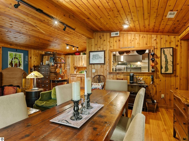 dining room with wood walls, rail lighting, wooden ceiling, and light wood-type flooring