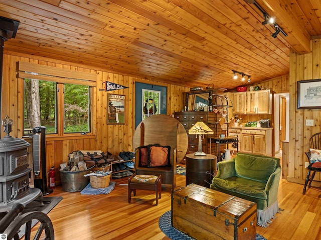 living room featuring a wood stove, rail lighting, wooden ceiling, light hardwood / wood-style floors, and wooden walls